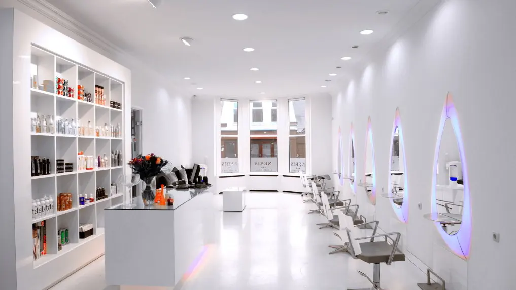 De salon van Neris Hairstudio: witte wanden, een kast met producten en een rij verlichte spiegels